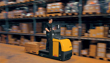 Worker driving Jungheinrich low-level order picker down aisle with blurred background